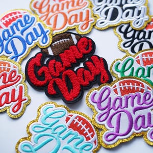 May include: A collection of nine embroidered iron-on patches with the text "Game Day" in various colours and styles. Each patch features a football graphic.