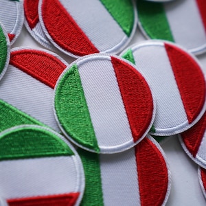 Può includere: Primo piano di diverse toppe rotonde ricamate con la bandiera italiana. Ogni toppa presenta uno sfondo bianco con strisce verticali verdi e rosse e un bordo bianco.