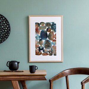May include: A wooden dining table with a light wood finish and a brown leather chair. A framed print of a watercolor painting of blue and brown stones hangs on the wall behind the table.