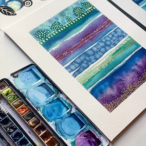 May include: A watercolor painting on paper with a layered abstract design. The painting features a variety of blues, purples, and greens with gold accents. The painting is framed and ready to hang.