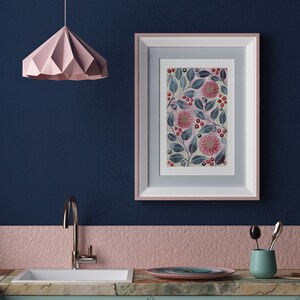 May include: A framed print of a floral design with pink flowers, green leaves, and red berries on a white background. The frame is pink and white and is hanging on a dark blue wall.