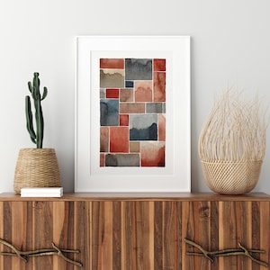May include: A framed abstract watercolor painting with geometric shapes in shades of red, brown, and blue. The painting is displayed on a wooden cabinet with a woven basket and a cactus plant.