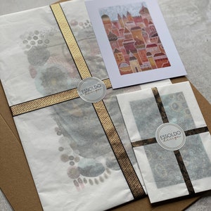 May include: Two white envelopes with black and gold ribbon tied around them. Each envelope has a round sticker with the text "Essoldo Design" in black text on a white background.