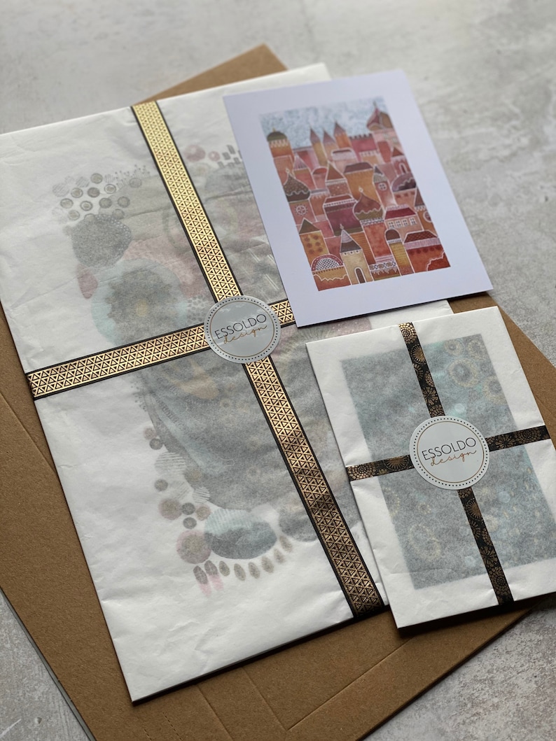 May include: Two white envelopes with black and gold ribbon tied around them. Each envelope has a round sticker with the text "Essoldo Design" in black text on a white background.