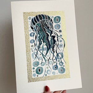 May include: A watercolor painting of a jellyfish with blue and green tones. The jellyfish is surrounded by gold dots and circles. The painting is framed with a gold border.