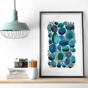 May include: Abstract watercolor painting of blue and teal circles and dots on a white background. The painting is framed in a black frame and is hanging on a white wall.