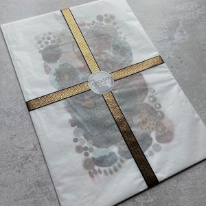 May include: A white envelope with a gold and black ribbon tied around it. The envelope has a sticker with the text "ESSOLDO Design" on it.
