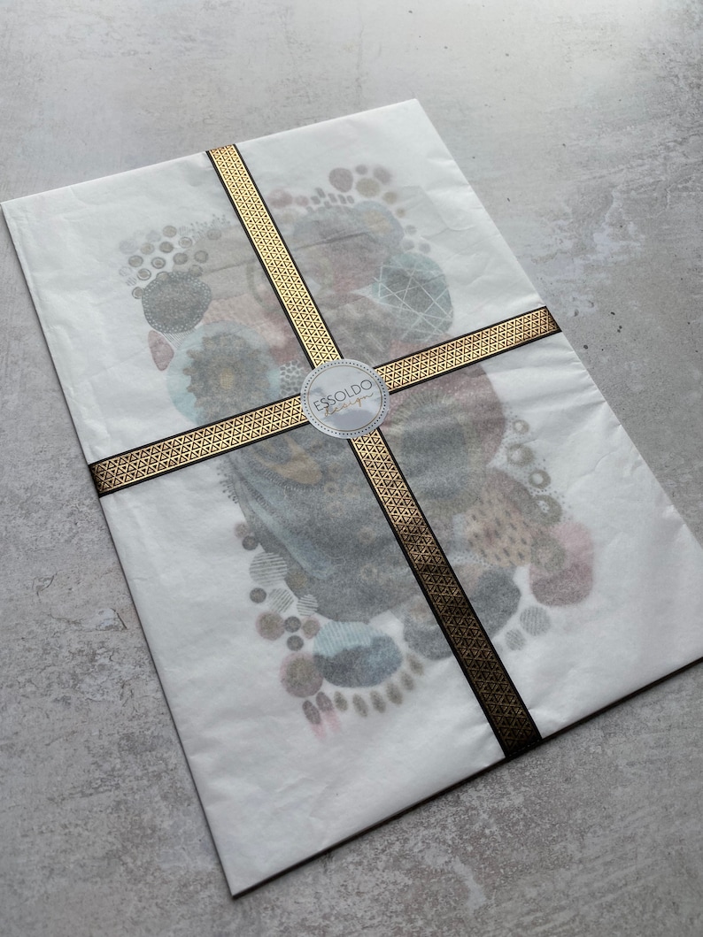 May include: A white envelope with a gold and black ribbon tied around it. The envelope has a sticker with the text "ESSOLDO Design" on it.