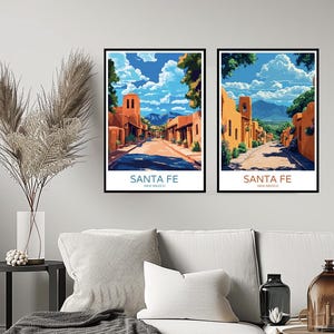 May include: Two framed prints depicting a street scene in Santa Fe, New Mexico. The prints feature colourful adobe buildings, a blue sky with white clouds, and a mountain range in the distance. The text "SANTA FE" and "NEW MEXICO" is printed below the image.