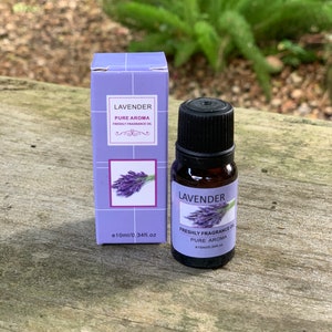 May include: A small glass bottle of lavender essential oil with a purple label that says "Lavender Pure Aroma Freshly Fragrance Oil e10ml/0.34fl.oz". The bottle is sitting on a wooden surface.