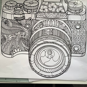 May include: Black and white line drawing of a camera with intricate patterns. The camera's body, lens, and dials are filled with detailed designs, creating a coloring book style image. The image is on a white background.