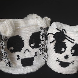 Puede incluir: Dos bolsas de golosinas de Halloween blancas tejidas a crochet. Una bolsa presenta un diseño de calavera negra y la otra tiene una araña negra. Ambas bolsas tienen un ribete blanco y negro. Las bolsas son perfectas para pedir dulces.
