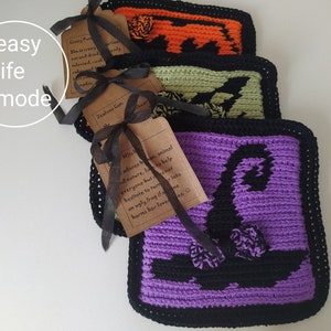 May include: Three crocheted Halloween-themed coasters in orange, green, and purple, each with a black border. The purple coaster features a witch hat design. Each coaster has a tag tied with a black ribbon.