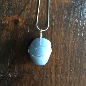 May include: A silver chain necklace with a light blue stone pendant wrapped in silver wire.
