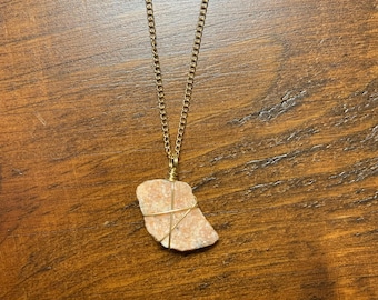 Puede incluir: Un collar de cadena dorada con un colgante de piedra rosa y blanca envuelto en alambre dorado.