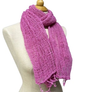 May include: A pink crocheted scarf with a delicate, open-weave pattern. The scarf is draped over a mannequin's neck and has a fringed edge.