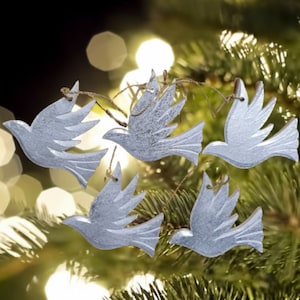 May include: Five silver dove ornaments hanging from a Christmas tree. The doves are made of wood and have a distressed finish.