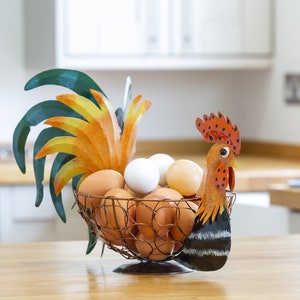 May include: A rooster-shaped wire egg holder with a colorful painted design. The holder is filled with brown and white eggs.