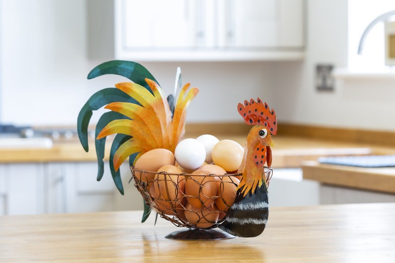 May include: A rooster-shaped wire egg holder with a colorful painted design. The holder is filled with brown and white eggs.