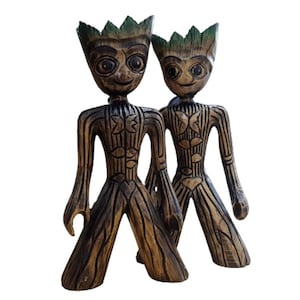May include: Two wooden figurines of a fictional character with green leaves on their heads. The figurines are standing side by side and are painted in shades of brown and black.