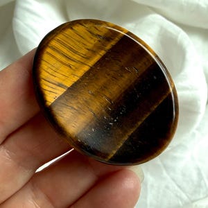 close-up tiger’s eye worry stone in hand with strong chatoyancy flash, grounding crystal for solar plexus confidence and clarity