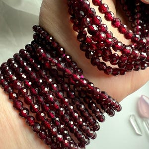 May include: A stack of red garnet gemstone bracelets. The bracelets are made of faceted beads and are strung on elastic.