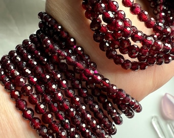 May include: A stack of red garnet gemstone bracelets. The bracelets are made of faceted beads and are strung on elastic.