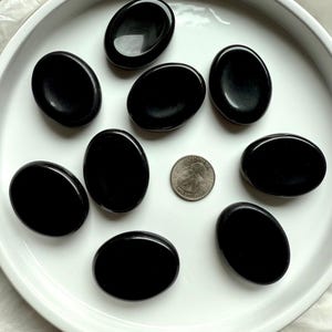 Smooth Black Obsidian worry stones on white tray with US quarter for scale – root chakra healing crystals for stress relief