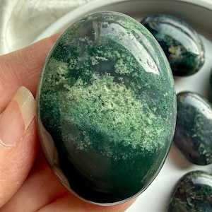 Close-up of moss agate palm stone in hand with translucent green inclusions, grounding stone for meditation and stress relief