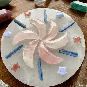 Crystal grid with Strawberry Quartz stars, Rose Quartz moons, Kyanite sticks, and Blue Lace Agate stars on wood table with additional healing crystals