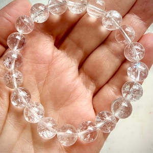 Clear Quartz crystal bracelet held in hand with transparent polished beads and light-catching flashes