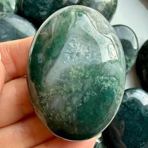 Hand holding moss agate palm stone showing natural dendritic patterns, soothing crystal for nervous system support