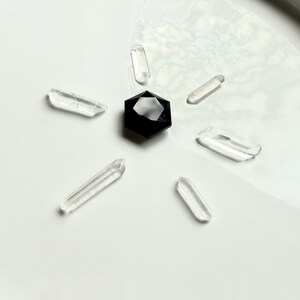 Black Obsidian hexagon crystal in sacred geometry grid layout, placed at center with six clear quartz points radiating outward for energy amplification