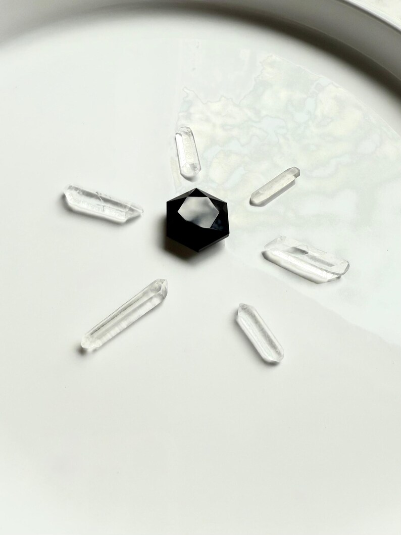 Black Obsidian hexagon crystal in sacred geometry grid layout, placed at center with six clear quartz points radiating outward for energy amplification