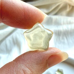 Mini Lemon Citrine star held between fingers showing its tiny size, translucence, and polished finish