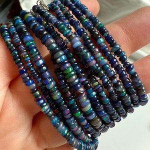 May include: A collection of beaded bracelets featuring small, round beads in shades of blue, green, and purple. The beads have an iridescent quality, creating a shimmering effect. The bracelets are strung together and appear to be made of a gemstone material.