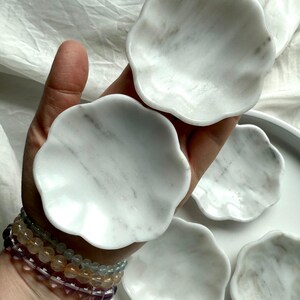 Two white marble daisy bowls shown in hand, with natural veining and smooth scalloped flower shape