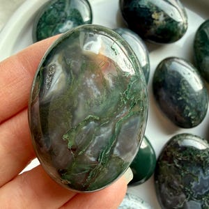 Polished moss agate palm stone resting in palm, earthy green crystal for emotional balance and grounding energy