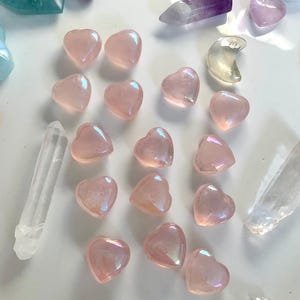 Angled view of aura rose quartz hearts with crystal points & celestial carvings — glowing pink stones for heart chakra healing & sacred decor