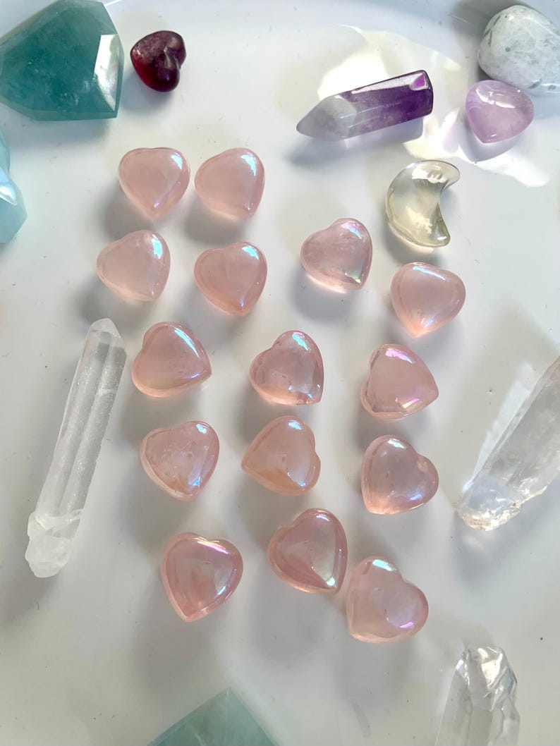 Angled view of aura rose quartz hearts with crystal points & celestial carvings — glowing pink stones for heart chakra healing & sacred decor