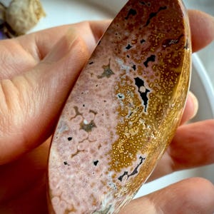 Side view of ocean Jasper moon crystal with peachy pink and golden yellow orbicular patterns held in hand for emotional healing