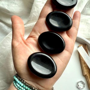 Black Obsidian palm stones lined up in hand – root chakra crystals for grounding, calming + daily energy clearing