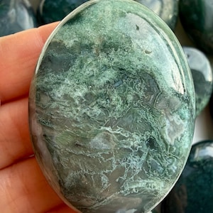 Close-up moss agate palm stone with translucent chalcedony and moss-like inclusions, soothing grounding crystal