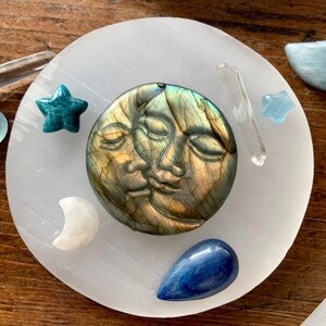 Overhead of labradorite sun and moon carving on round selenite charging plate surrounded by mini crystal stars and moons
