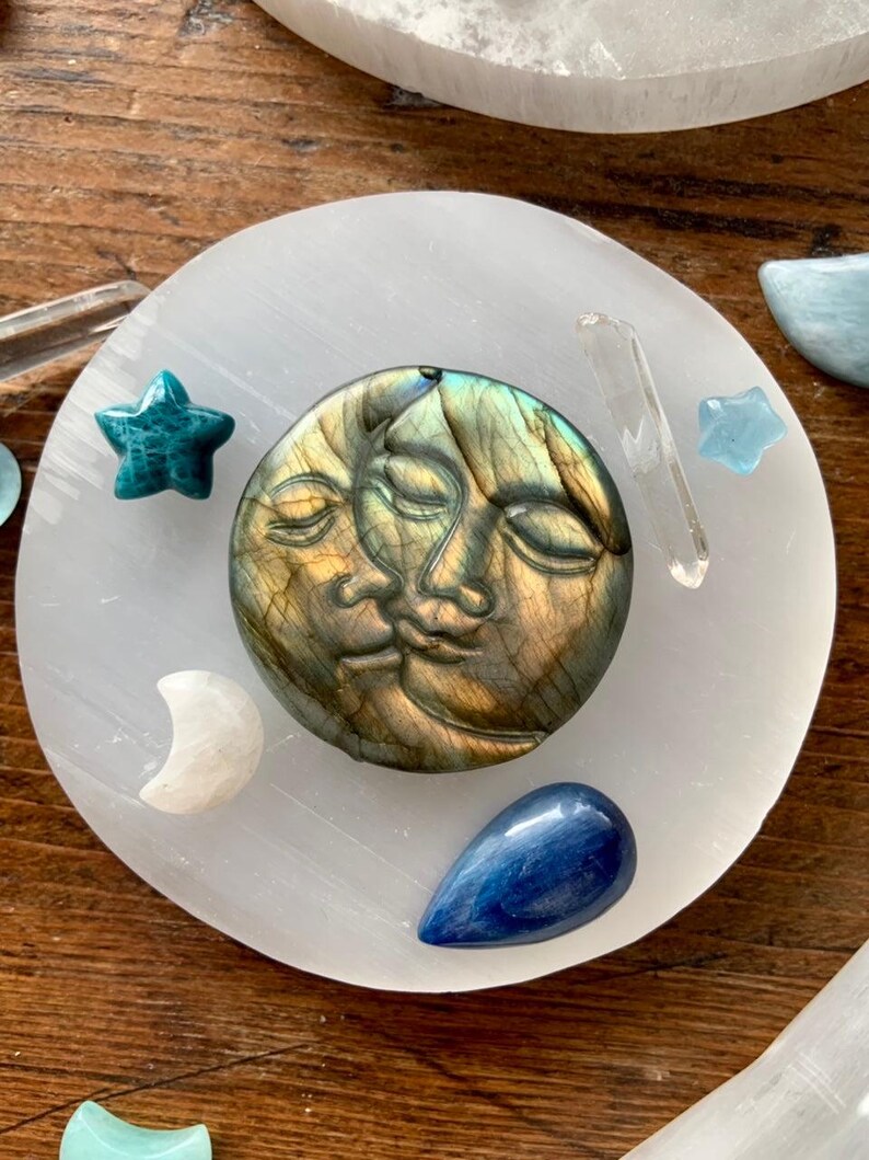 Overhead of labradorite sun and moon carving on round selenite charging plate surrounded by mini crystal stars and moons