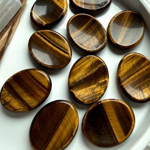 group of tiger’s eye worry stones scattered on marble surface, polished crystals for grounding stability and energy protection