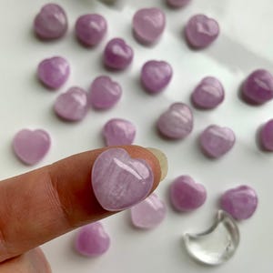Mini Pink Kunzite heart shown on a fingertip for scale with more hearts in the background — tiny crystal carving for emotional healing & crystal gifting.