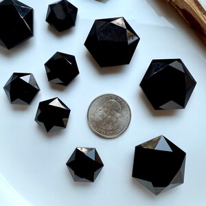Faceted Black Obsidian hexagon crystal shown in two sizes beside a quarter for size reference, glossy black sacred geometry carving