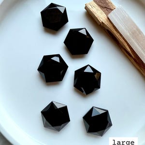 Overhead view of multiple large faceted Black Obsidian hexagon crystals in a white dish, polished sacred geometry carvings for grounding and protection