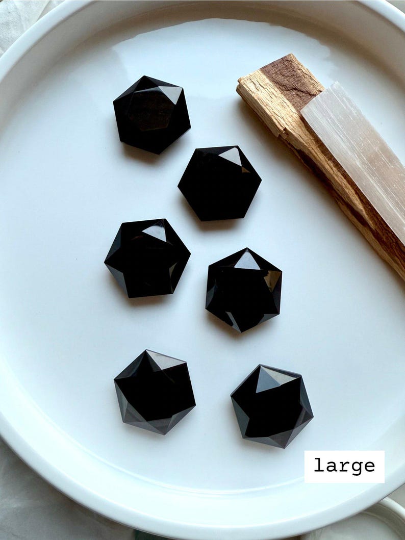 Overhead view of multiple large faceted Black Obsidian hexagon crystals in a white dish, polished sacred geometry carvings for grounding and protection